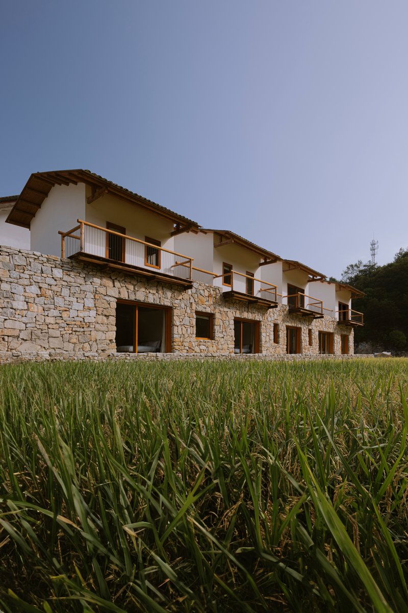 Stone wall facade with timber-framed balconies rising from a grassy rice paddy at dusk