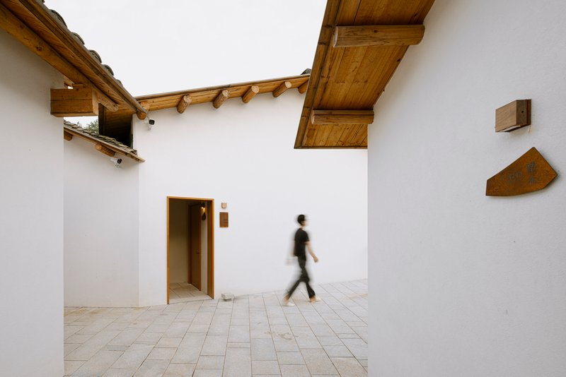 Open courtyard with white walls and exposed timber eaves as a figure walks across stone pavers