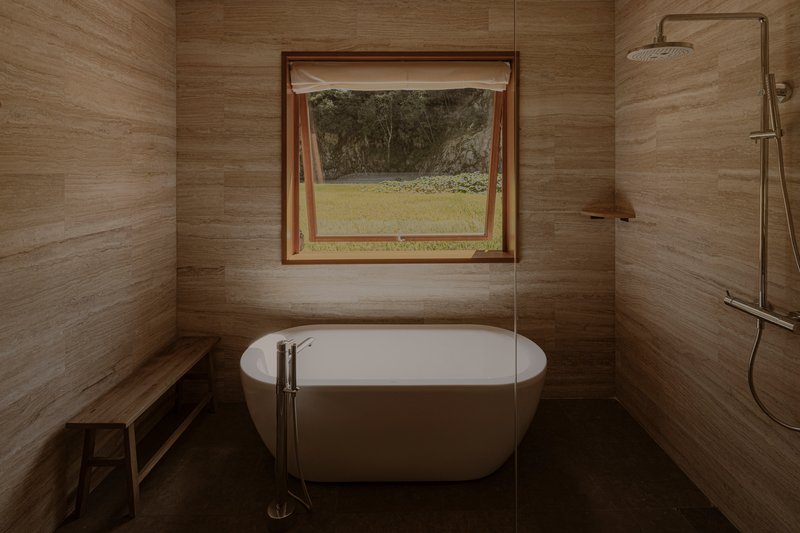 Bathroom with freestanding tub, wood-grain tile walls and casement window opening to green lawn