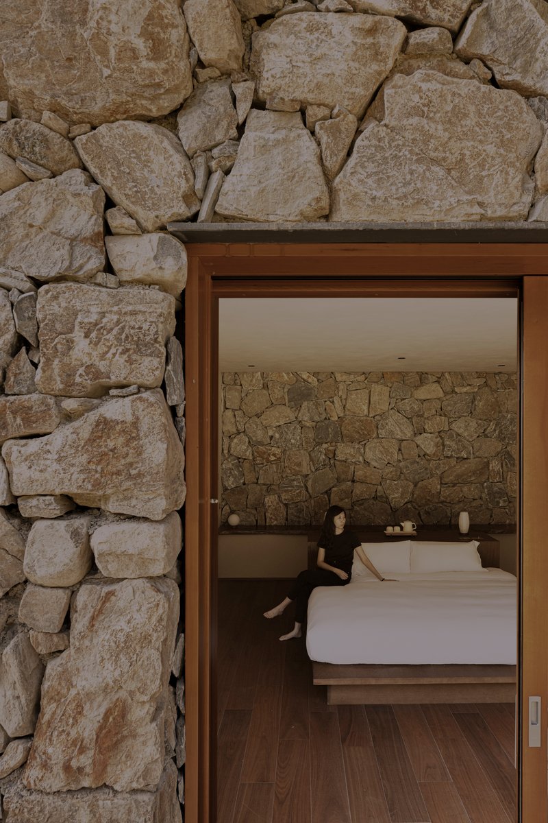 Sliding glass door framed by dry-stacked stone walls revealing a bedroom with exposed rock headboard