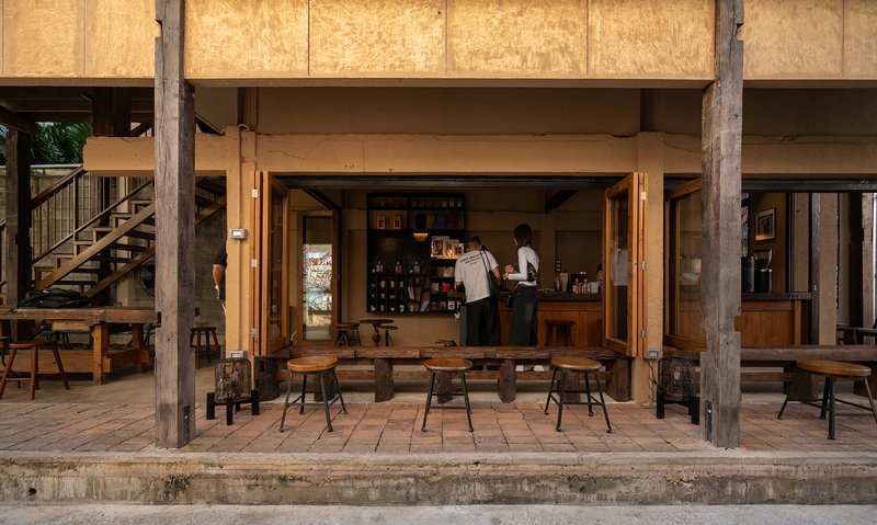 Ground-floor cafe counter with folding timber doors opening to outdoor seating under reclaimed timber beams