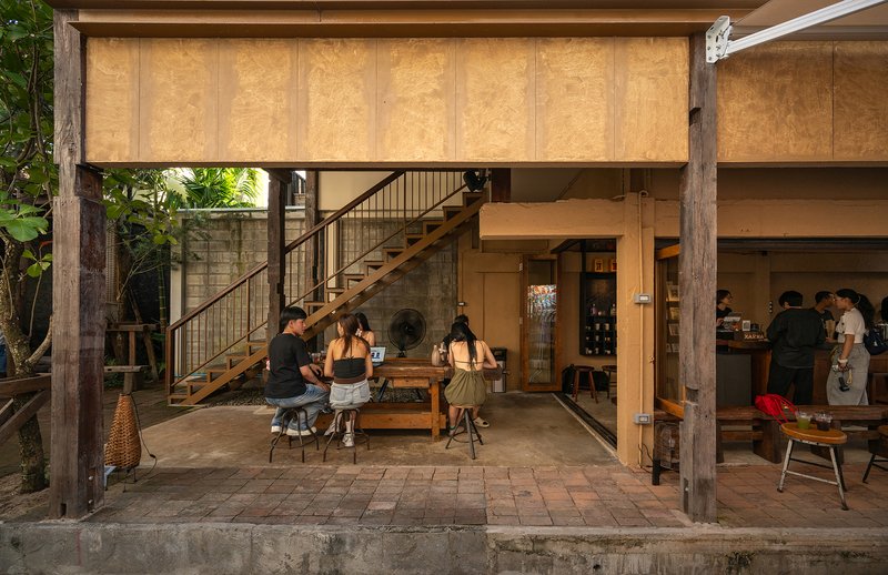 Covered terrace with timber staircase and plywood ceiling panels overlooking courtyard seating at dusk