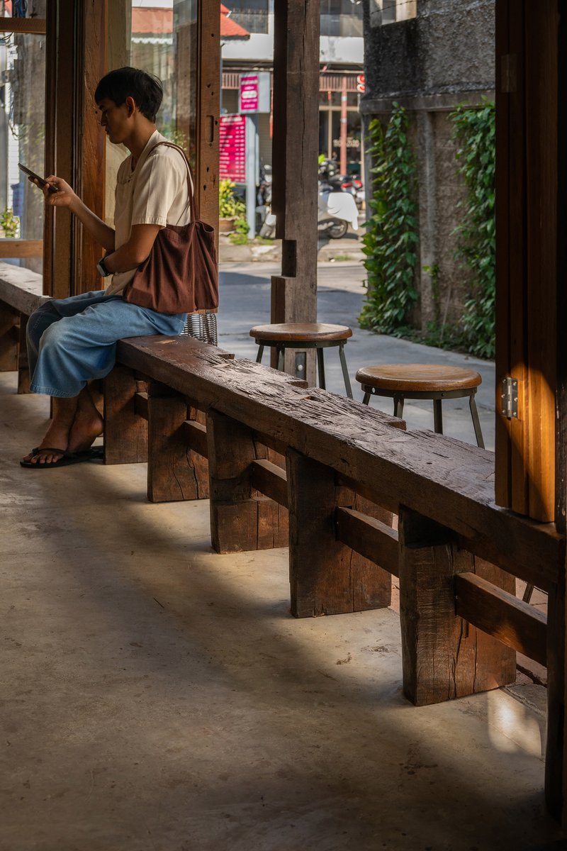 Timber bench and stools along the interior threshold where a person sits reading in natural daylight
