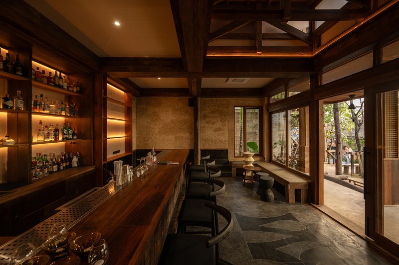 Interior bar with backlit shelving, timber post-and-beam structure and glazed doors overlooking a planted garden