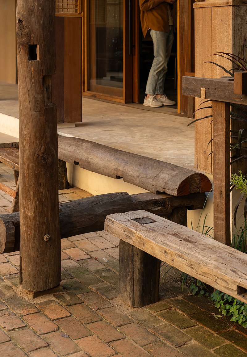 Reclaimed timber bench and columns on a brick paved terrace with a person entering through glazed doors
