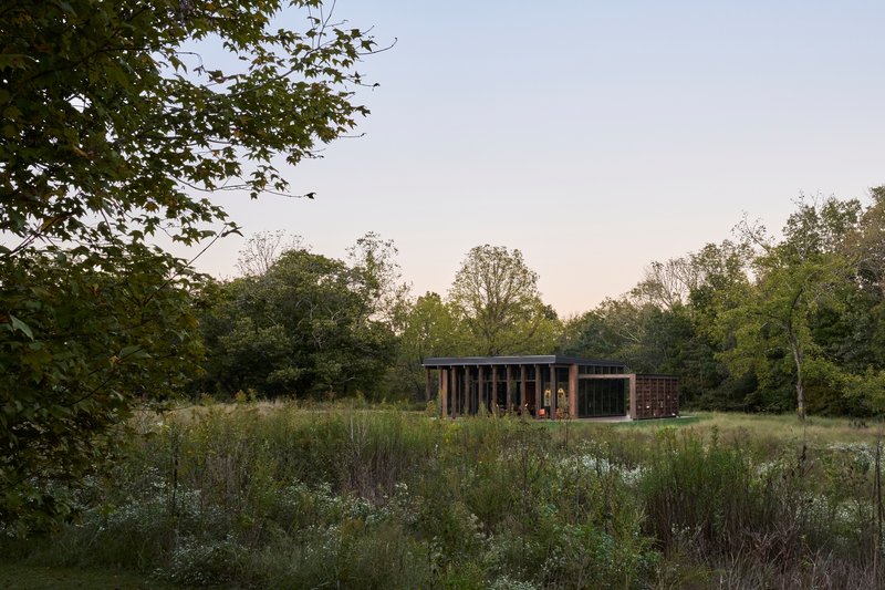 Pavilion with vertical timber cladding and slatted screens set in a wildflower meadow at dusk