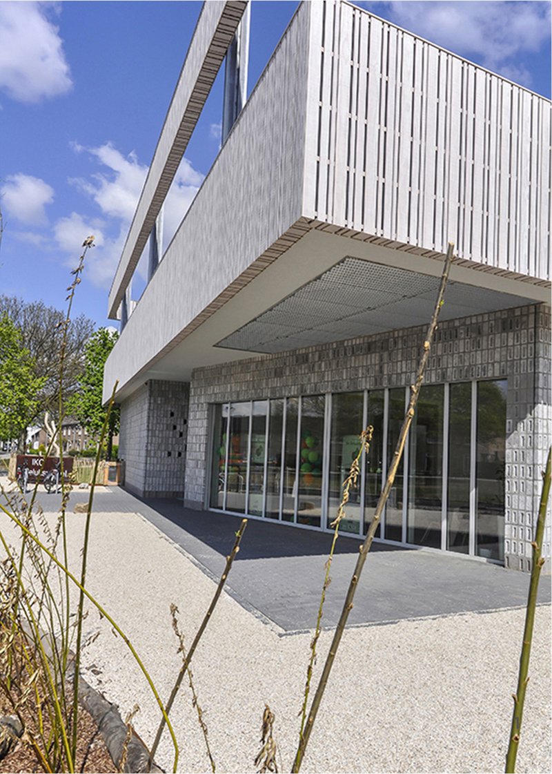 The entrance combines textured masonry, deep overhangs, and transparent glazing to create a welcoming educational environment.