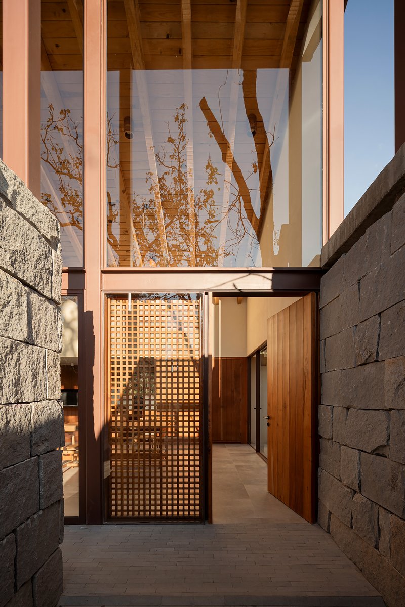 Entry passage with latticed timber gate between textured concrete walls under a timber-clad soffit at sunset