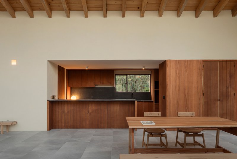 Open kitchen with walnut cabinetry and dark countertop beneath a timber-beamed ceiling and white walls