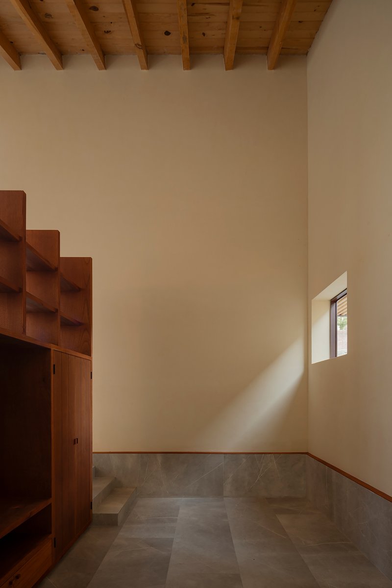 Corner room with stepped timber shelving and sunlight streaming through a deep-set window onto grey floor