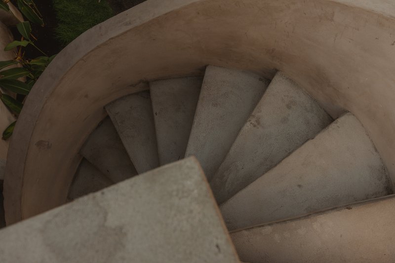 Top-down view of a circular concrete staircase descending with palm foliage visible at the edge