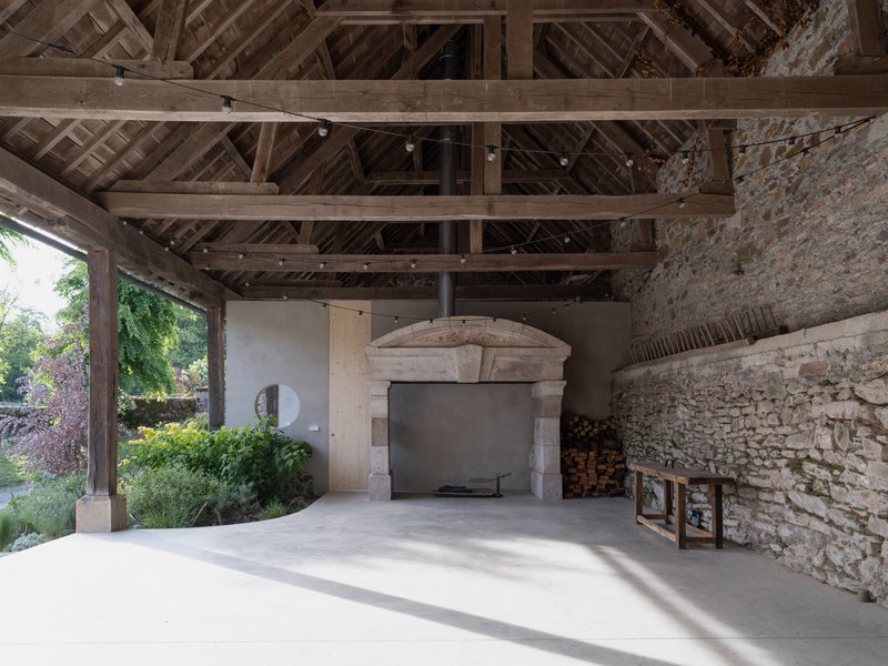 Exposed timber roof trusses over stone fireplace with original masonry walls and stacked firewood