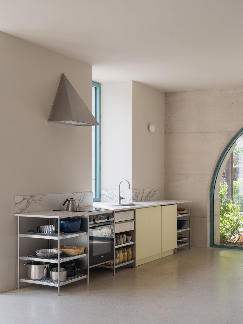 Kitchen counter with marble backsplash, open metal shelving, and conical metal range hood under soft daylight