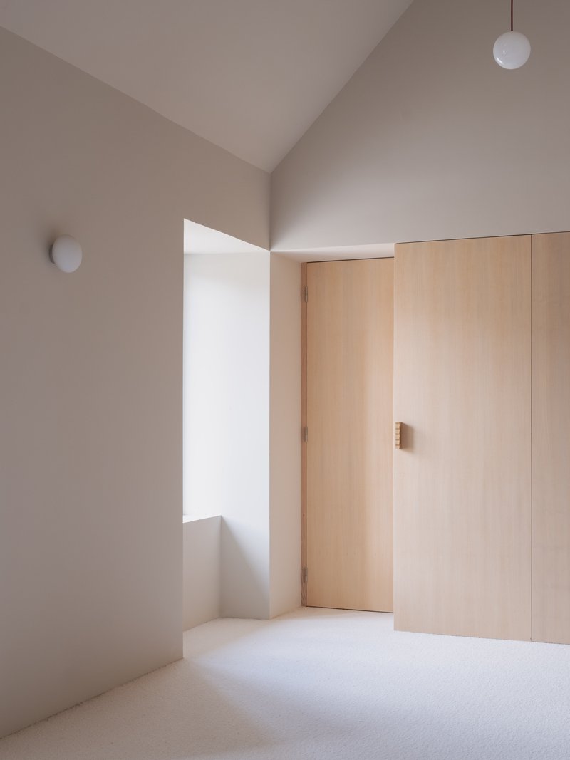 Vaulted bedroom interior with plywood wardrobe doors and round wall sconce in pale plaster walls