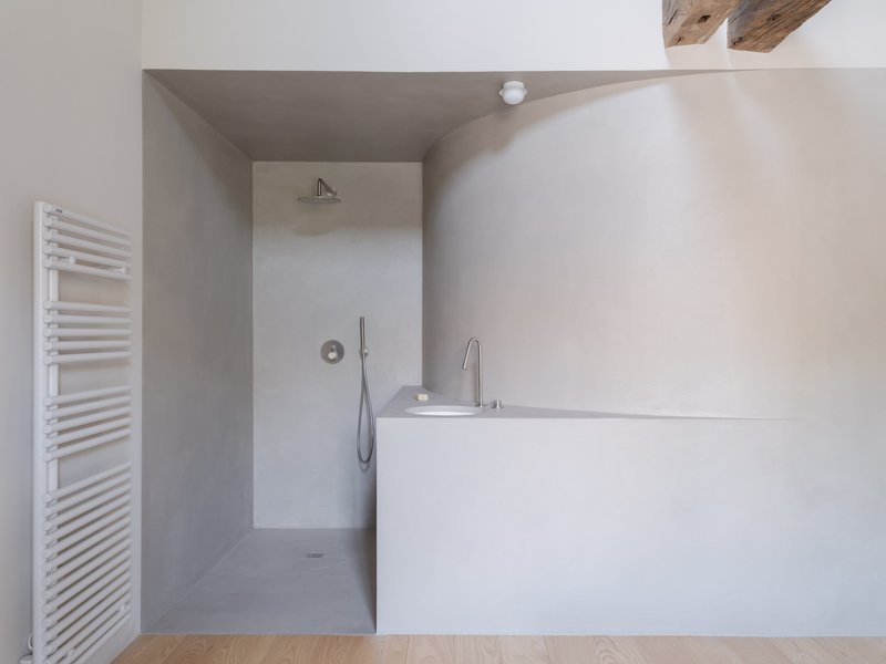 Bathroom with tadelakt-finished bathtub and walk-in shower alcove under exposed timber beams