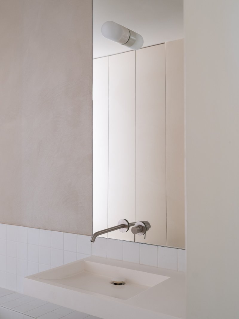 Bathroom vanity with undermount sink and wall-mounted taps below a frameless mirror and cylindrical sconce