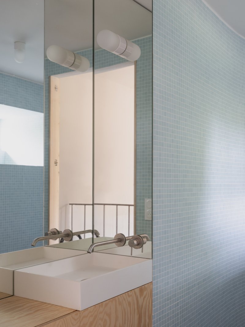 Bathroom mirror reflecting pale blue mosaic tile wall and handrail with timber vanity below