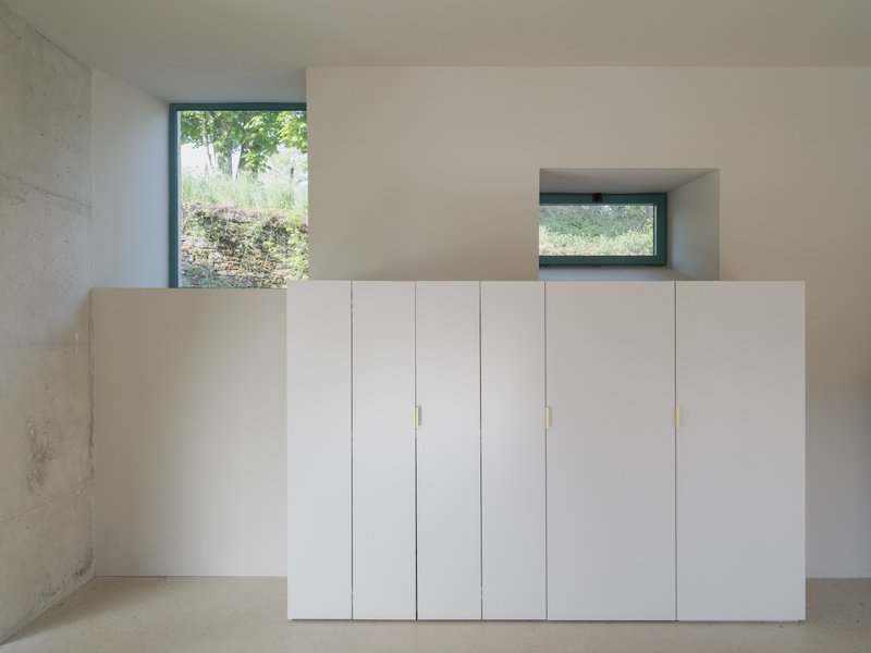 White storage cabinet with brass pulls beneath deep window looking onto garden with stone wall
