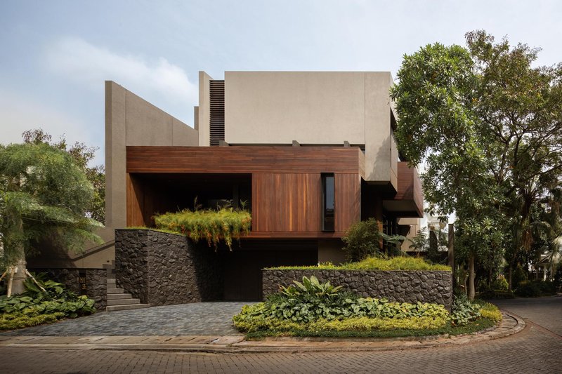 Street view of the cantilevered timber-clad volume above a stone retaining wall with planted beds