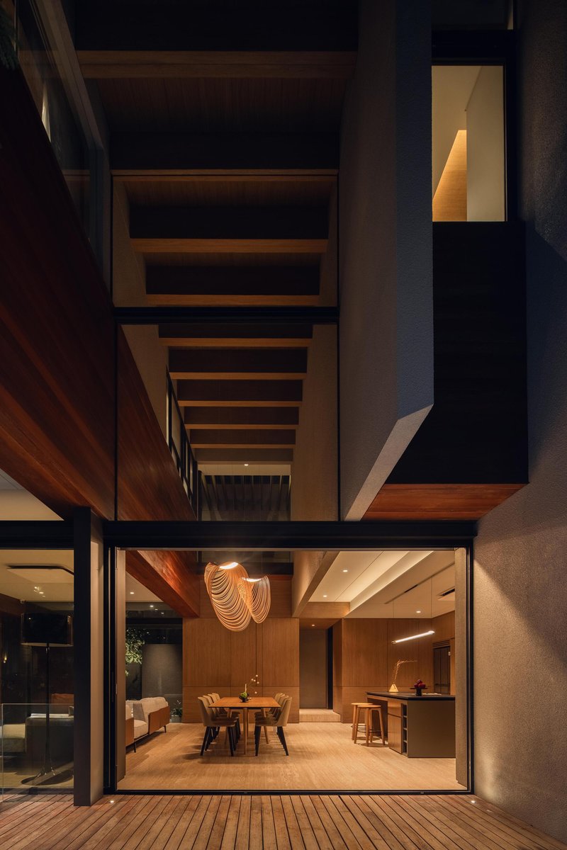 Courtyard view at dusk showing stacked volumes with timber screens and illuminated interior dining space
