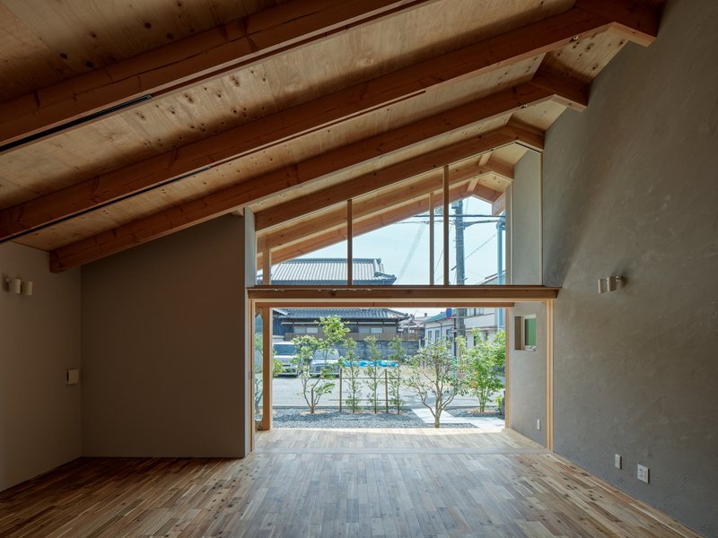 Interior view through the timber-framed opening toward the planted courtyard with young trees in daylight