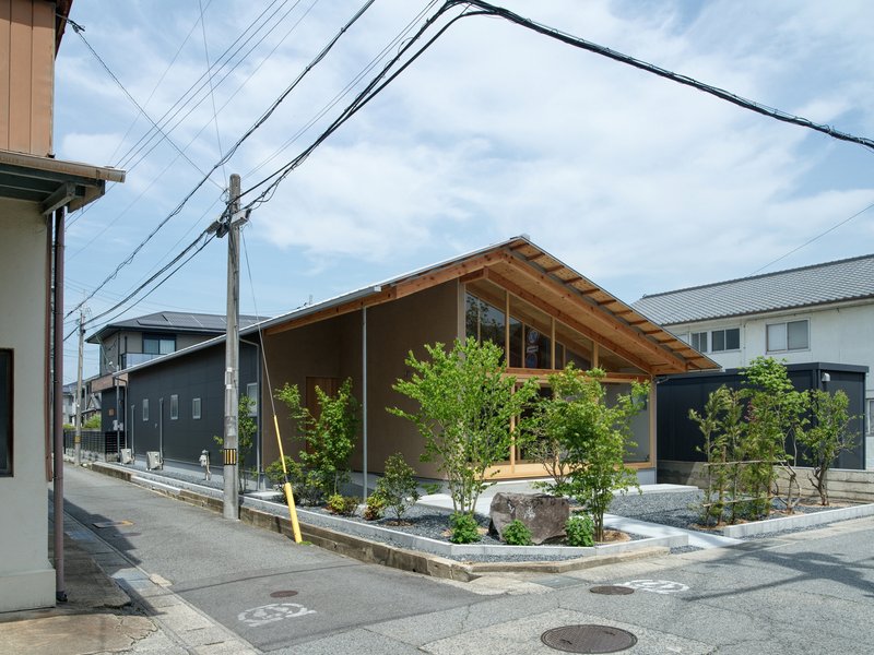 Street view of a low-slung residence with exposed timber roof and planted front courtyard under cloudy sky
