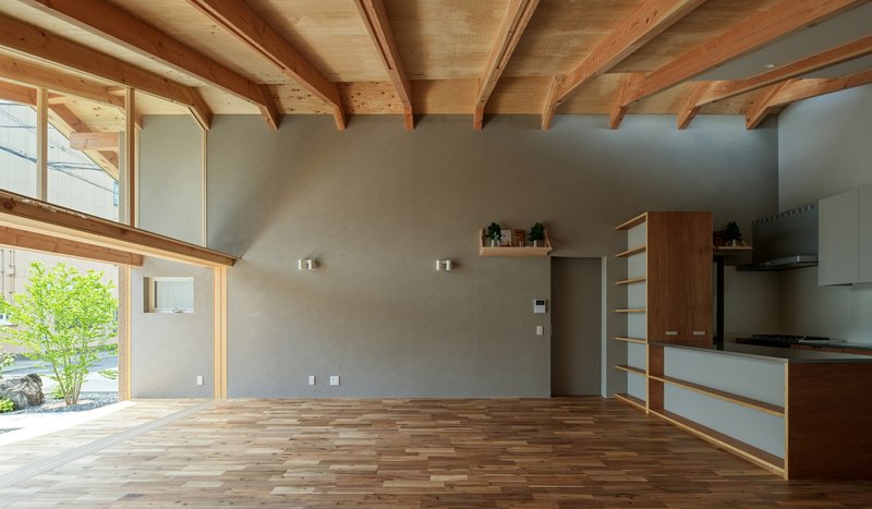 Open living space with exposed timber rafters, grey plaster walls, and timber and white kitchen cabinetry