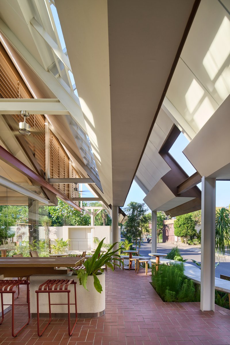 Covered outdoor terrace with herringbone brick floor and concrete columns opening to planted courtyard