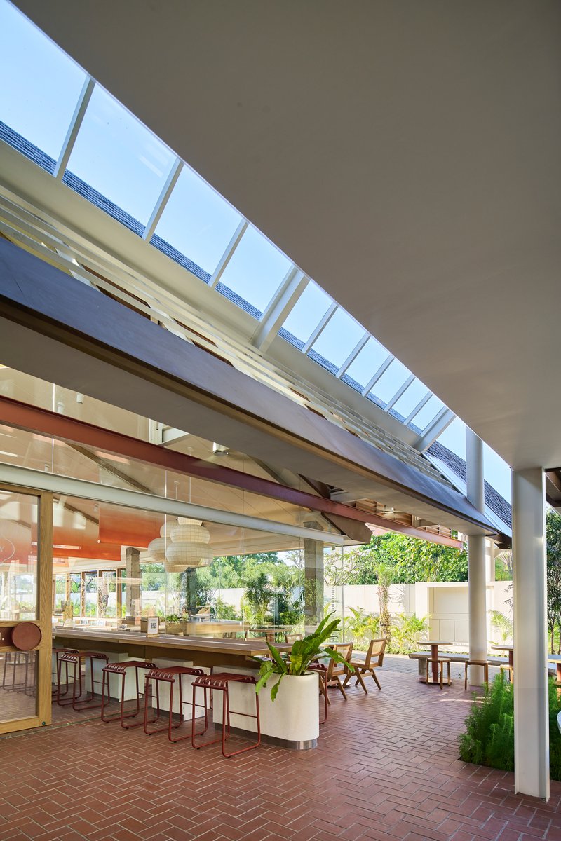 View through continuous clerestory glazing above terrace seating with outdoor brick paving and greenery