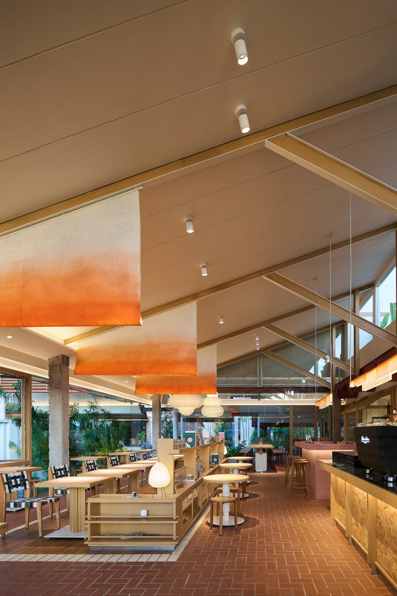Interior dining space with orange gradient ceiling panels, timber beams, and terracotta herringbone floor