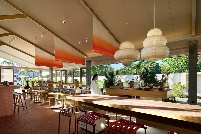 Dining area with long timber tables, globe pendant lights, and views to planted courtyard beyond