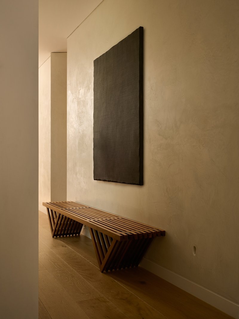 Hallway with slatted timber bench below a dark rectangular panel on the plastered wall
