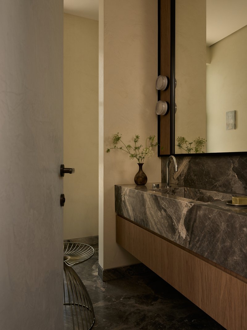 Bathroom with dark stone floating vanity, vertical mirror, and wire stool on stone tile floor