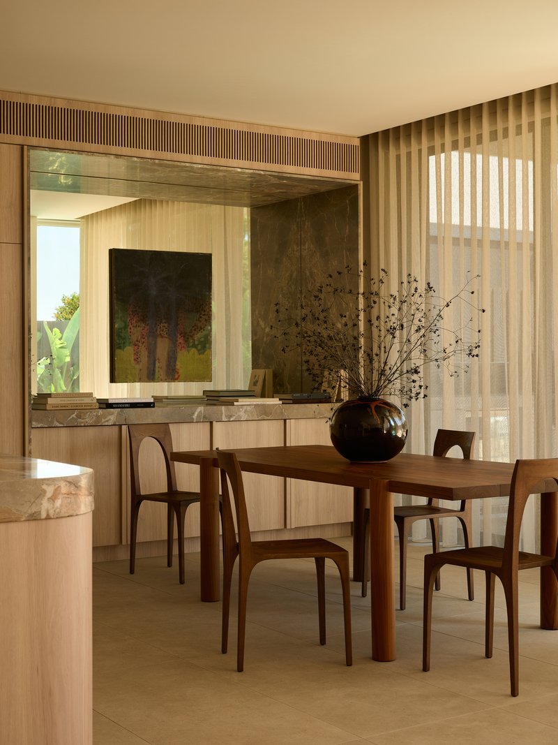 Dining area with timber table and chairs framed by vertical slat screens and sheer drapes