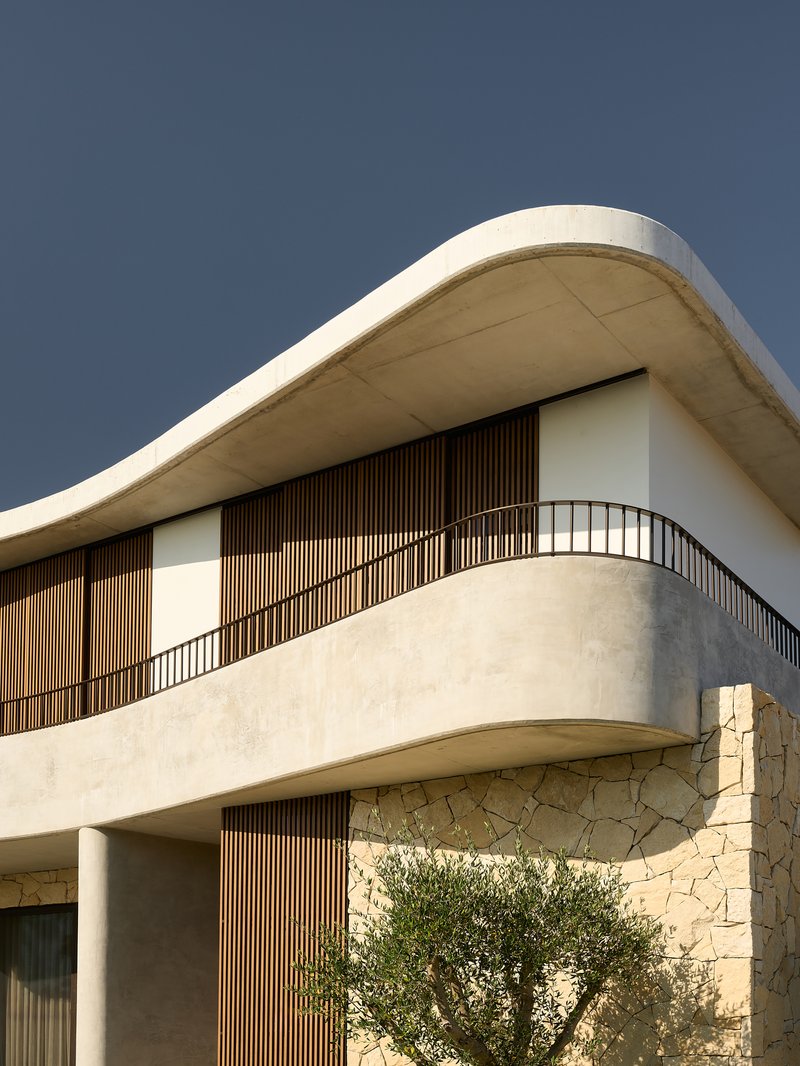 Curved balcony with vertical timber screens and stone cladding beneath an overhanging concrete soffit against a dark sky