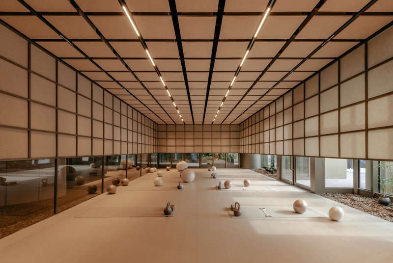 Long exercise room with translucent gridded walls and ceiling, scattered equipment on pale floor under linear lighting