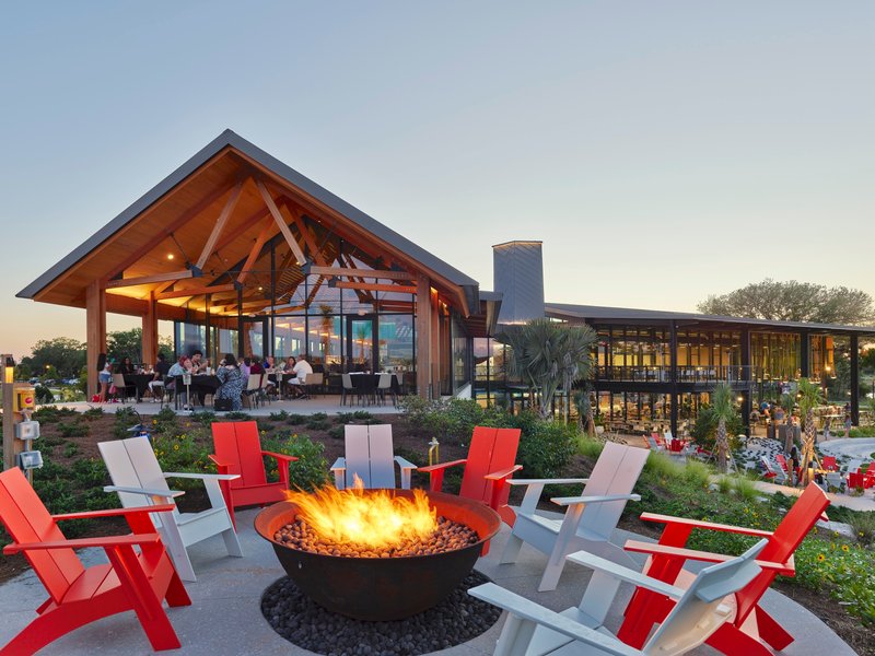 Outdoor fire pit surrounded by red and white chairs with covered dining pavilion at dusk