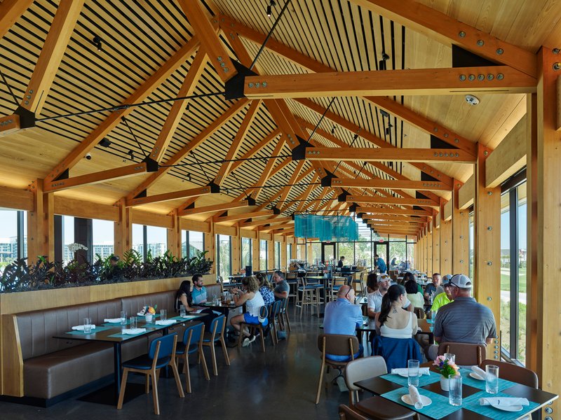 Dining hall with exposed timber trusses and slatted ceiling panels over tables filled with seated guests