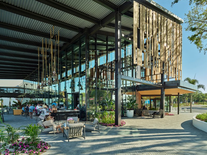 Covered outdoor dining terrace with steel columns, corrugated metal roof and vertical timber screen under blue sky