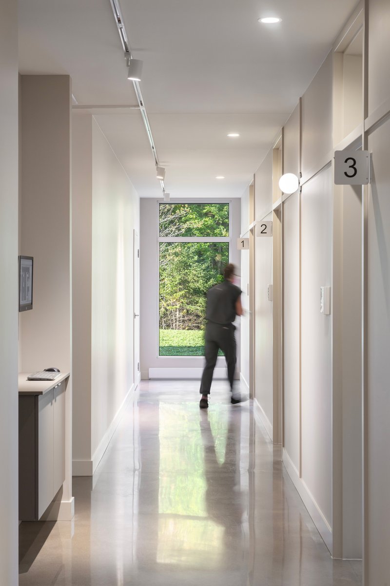 White corridor with polished concrete floor and figure in motion passing a large window to green trees