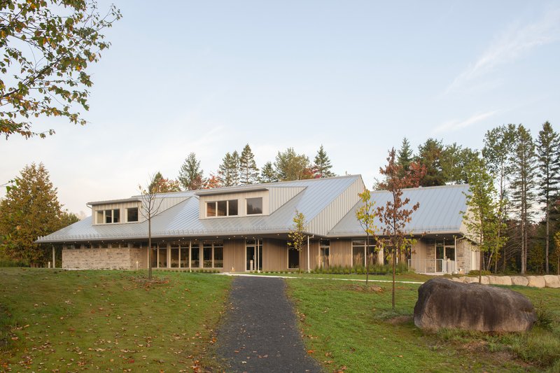 Front elevation with stone masonry walls, dormers, and metal roofline approached by a paved drive