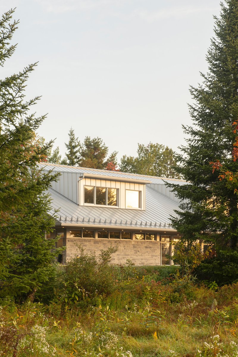 Rear view of the stone and vertical siding volumes framed by evergreen and deciduous trees