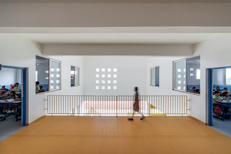 Interior corridor with orange floor tiles, metal railing, and grid of square windows as a student walks past