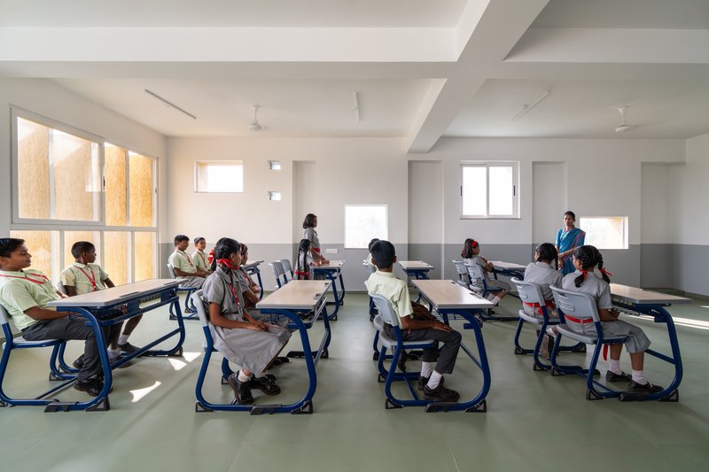 Classroom with blue chairs and grey floor as students sit at tables under morning sunlight