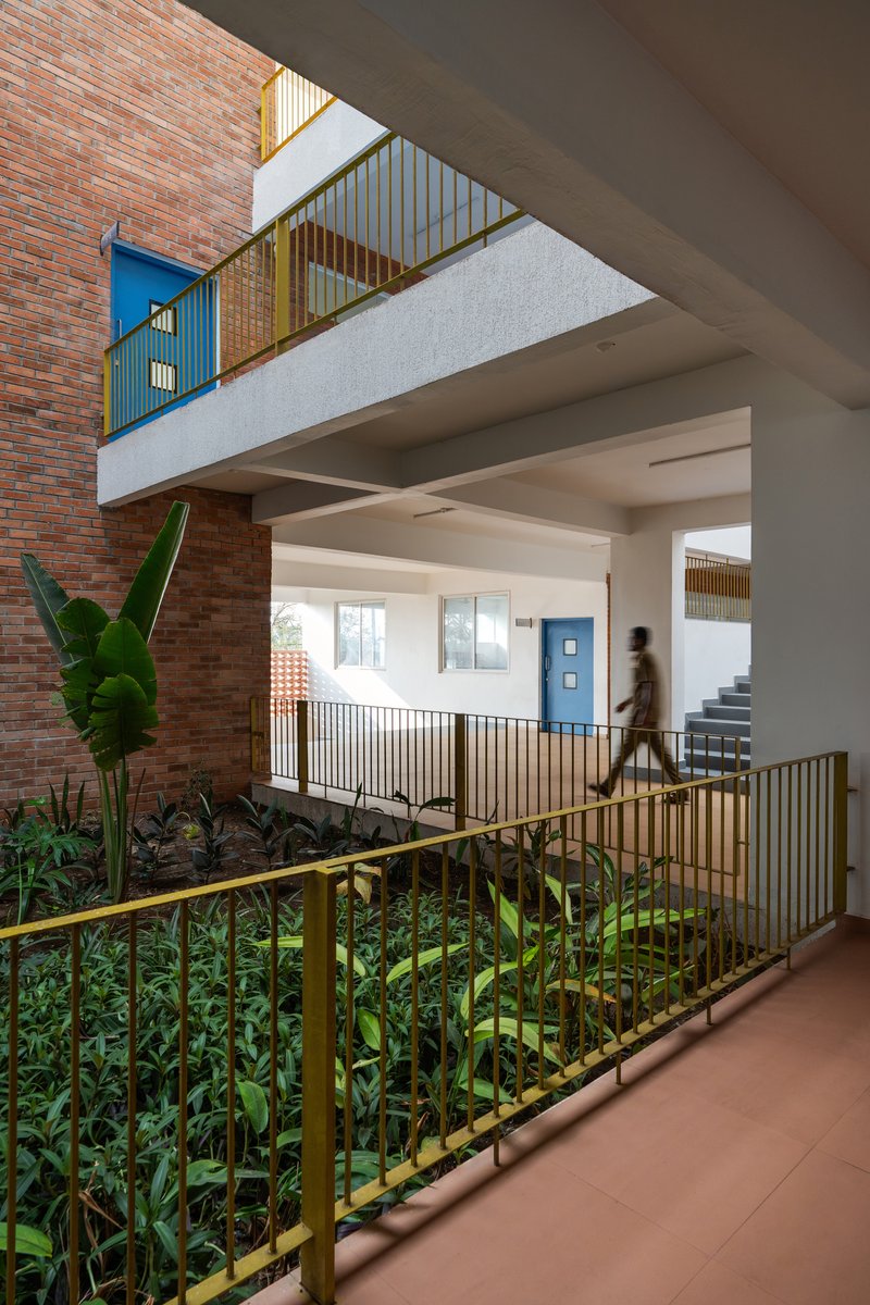 Multi-level atrium with planted beds, yellow metal railings, and exposed brick wall beside banana leaves