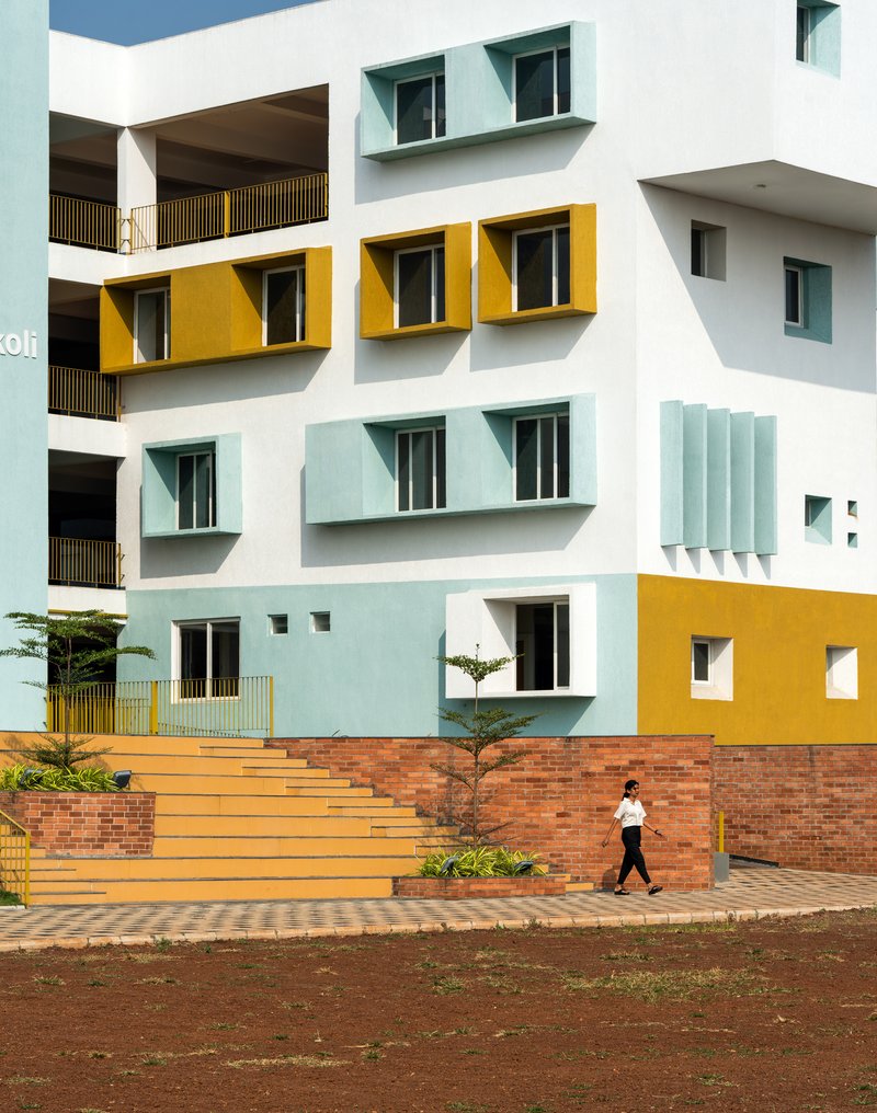 Facade with yellow and pale blue protruding window boxes above a brick retaining wall and student