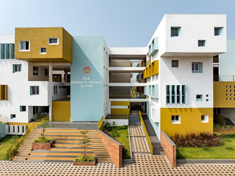 Entrance court with wide brick steps, planted beds and tiered facade volumes in yellow, white and pale blue