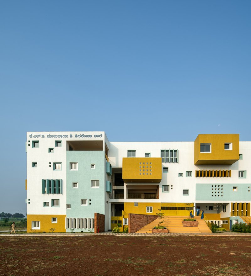 Front elevation showing stacked volumes in white, yellow and pale blue with cantilevered upper floors under clear sky
