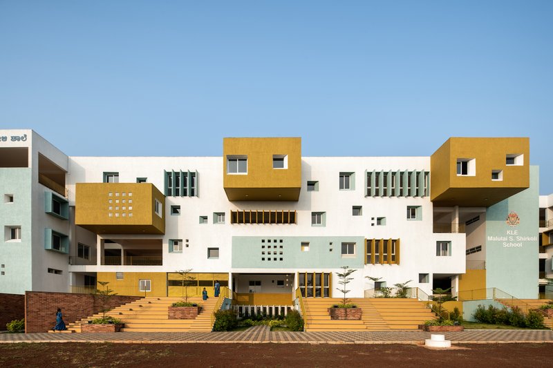 Front facade with white walls, cantilevered mustard volumes and tiered steps under clear blue sky