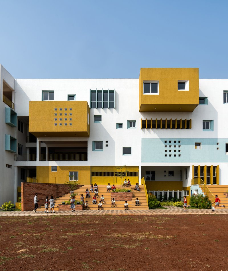Facade overlooking the steps and courtyard filled with children in uniform gathering outside